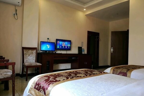 A hotel room with two beds, a desk with a computer, a chair, and a television.
