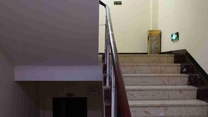 A staircase with marble steps and a metal handrail, leading to a landing with a marble column and an emergency exit sign. - Jinquan Business Hotel (Jinping)