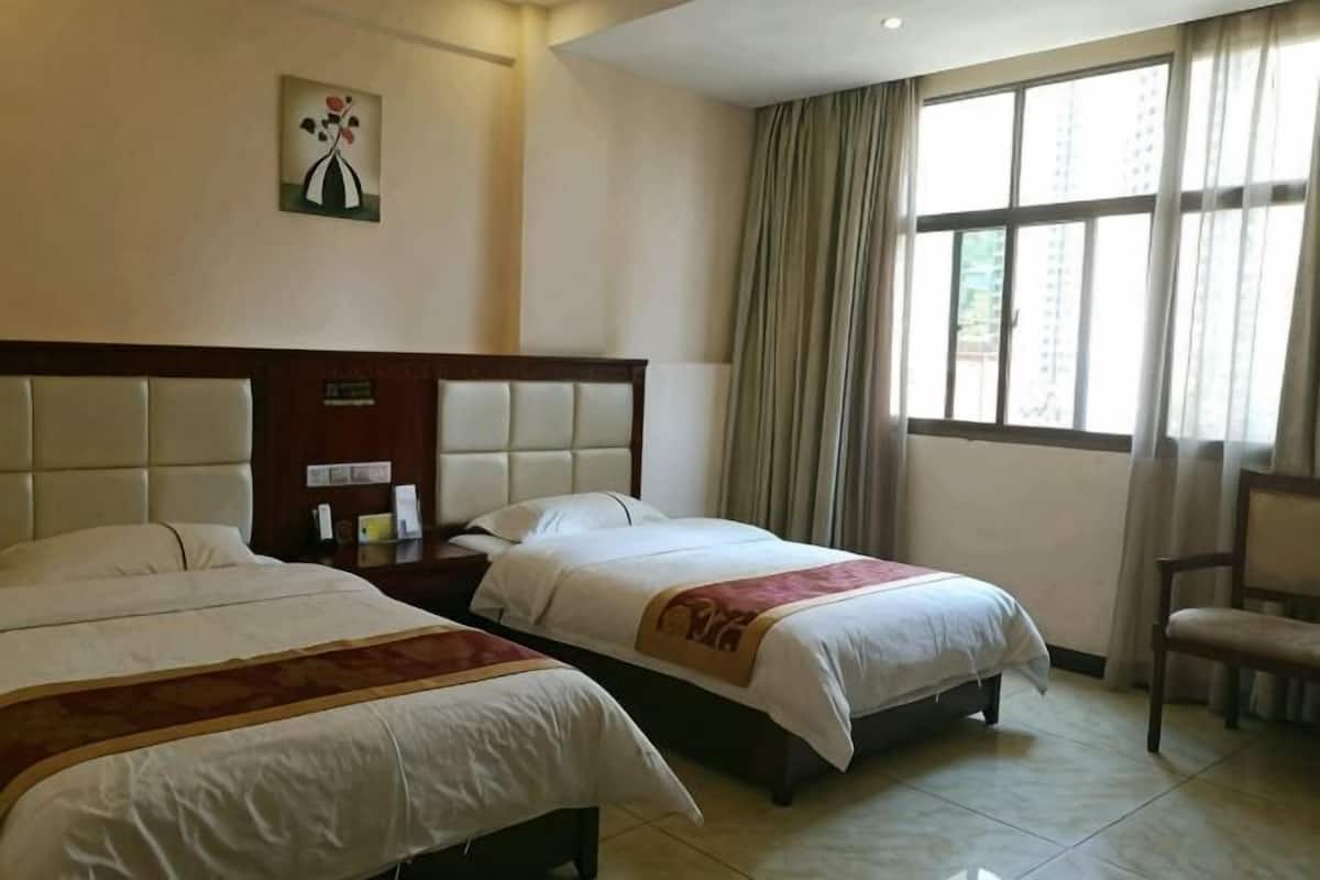 Habitación de hotel con dos camas, una mesita de noche, una silla y un ventanal con cortinas.