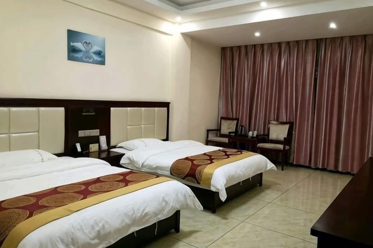 Habitación de hotel con dos camas, un escritorio, una silla, un ventanal con cortinas y un cuadro en la pared.