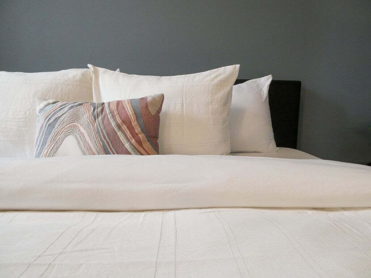 A neatly made bed with white linens and a colorful striped pillow.
