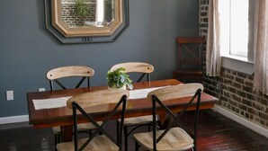 Un comedor con una mesa y sillas de madera, un espejo grande en la pared y un muro de ladrillo.