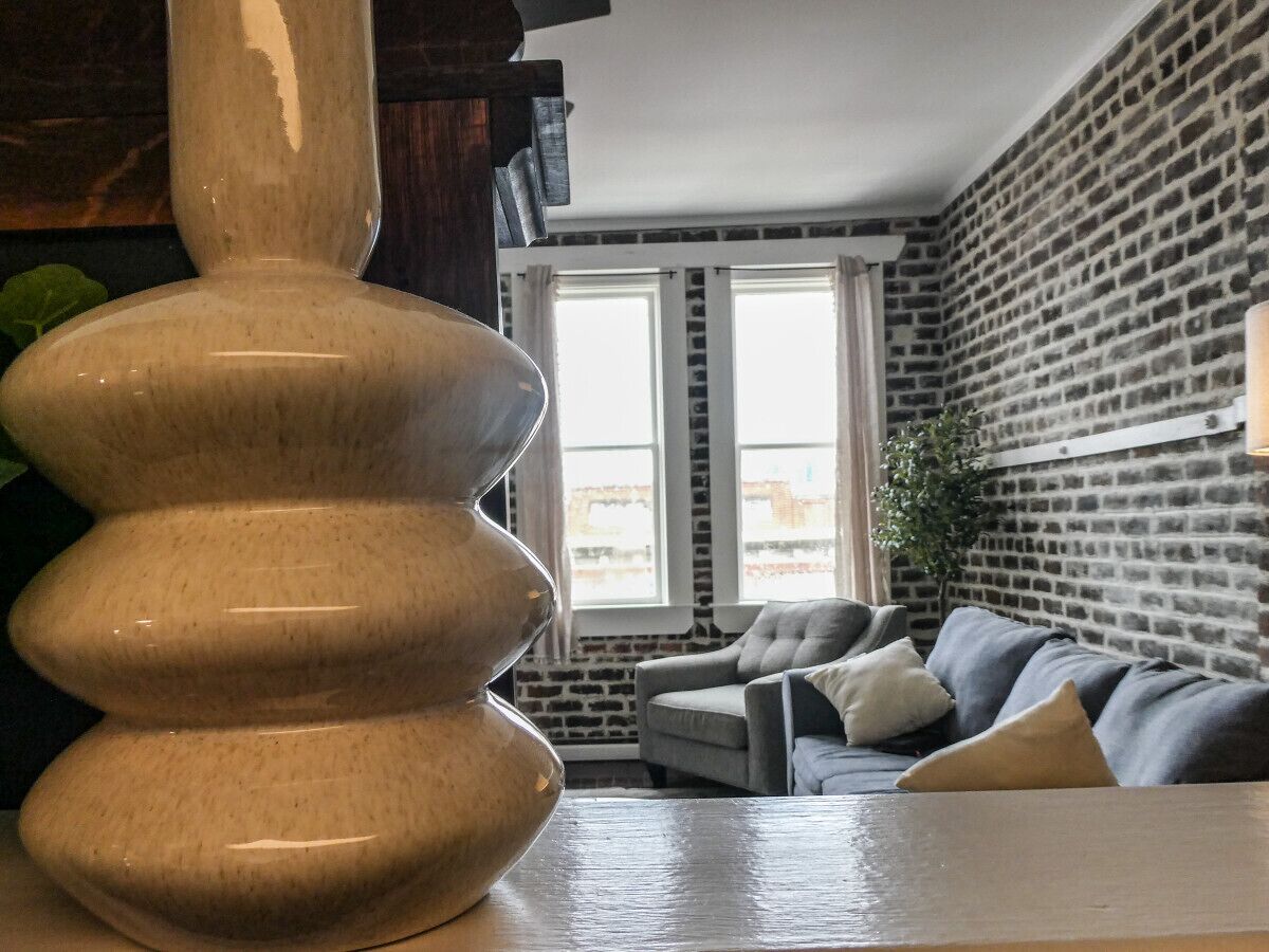 Un salon moderne avec une grande sculpture en bois, un canapé gris et un mur en briques.