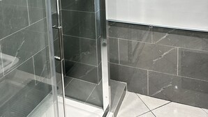 A modern bathroom with dark marble tiles, a glass shower enclosure, and a white wall. - Guest&Rest Elite  (London)
