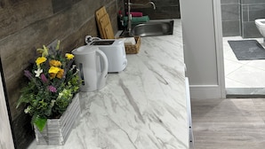 A modern kitchen with white cabinets, a marble countertop, a built-in sink, and a small plant arrangement. - Guest&Rest Elite  (London)