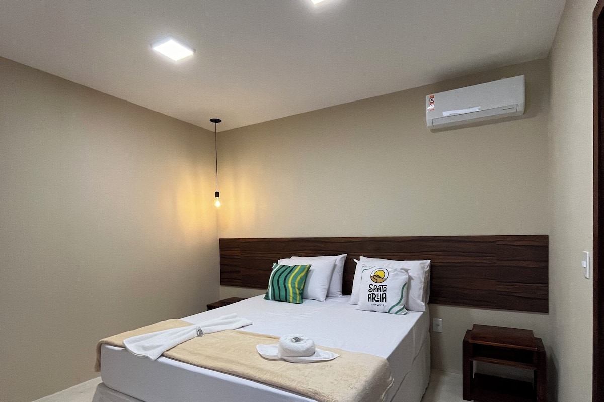 A hotel room with a bed, bedside tables, an air conditioning unit, and a ceiling light.
