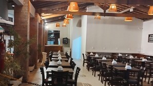A dining area with tables and chairs, overhead lighting, and a brick wall. - Santa Areia Lençóis Pousada (Santo Amaro do Maranhão)