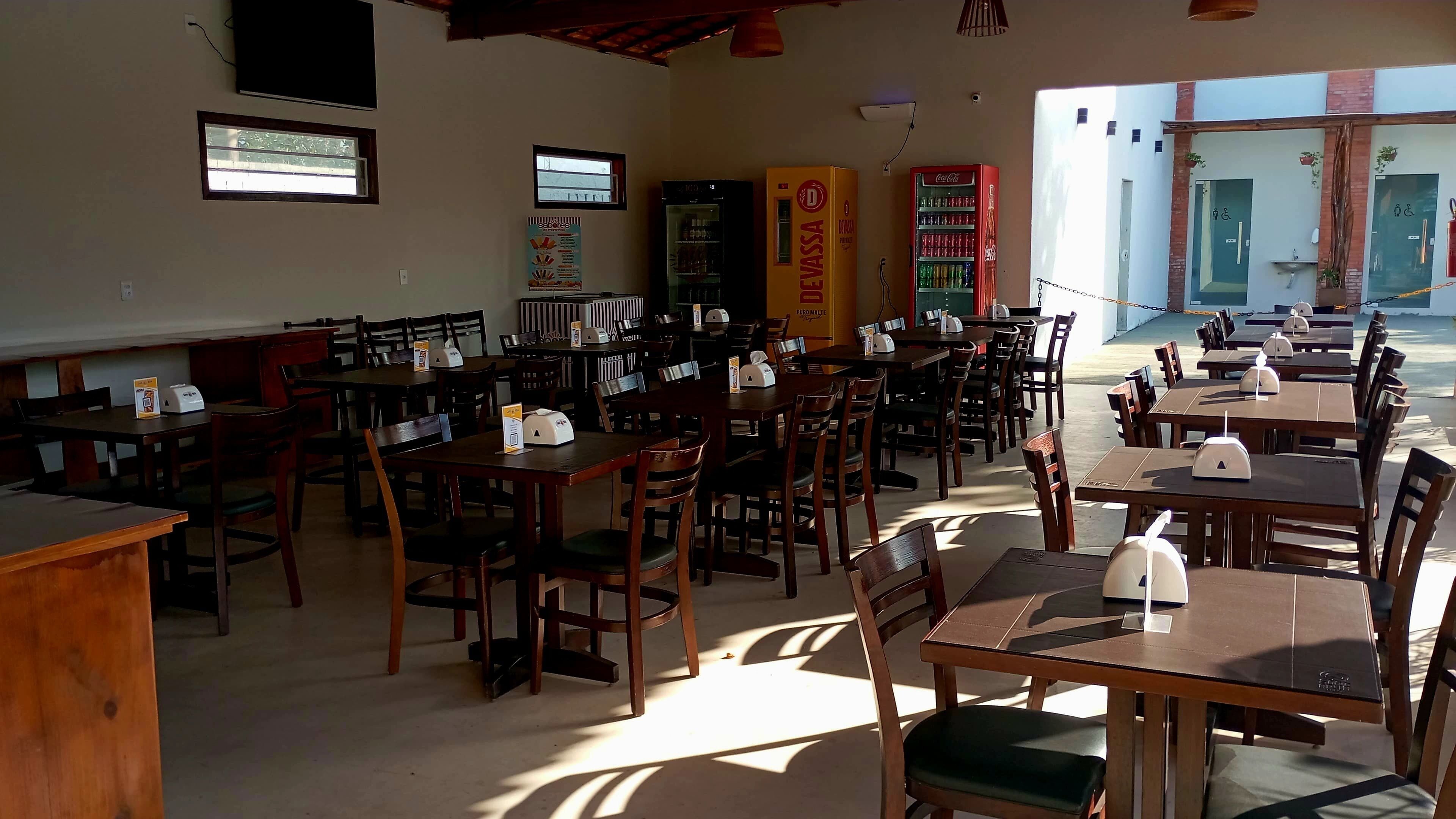 A restaurant with multiple wooden tables and chairs, a Coca-Cola refrigerator, and a menu board.