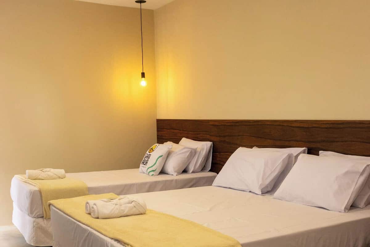 A hotel room with four single beds, each with a white bedspread and a yellow towel.
