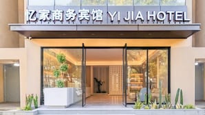 Esterno dell'hotel Yi Jia Hotel con facciata moderna, grande ingresso in vetro e una zona salotto interna con piante.