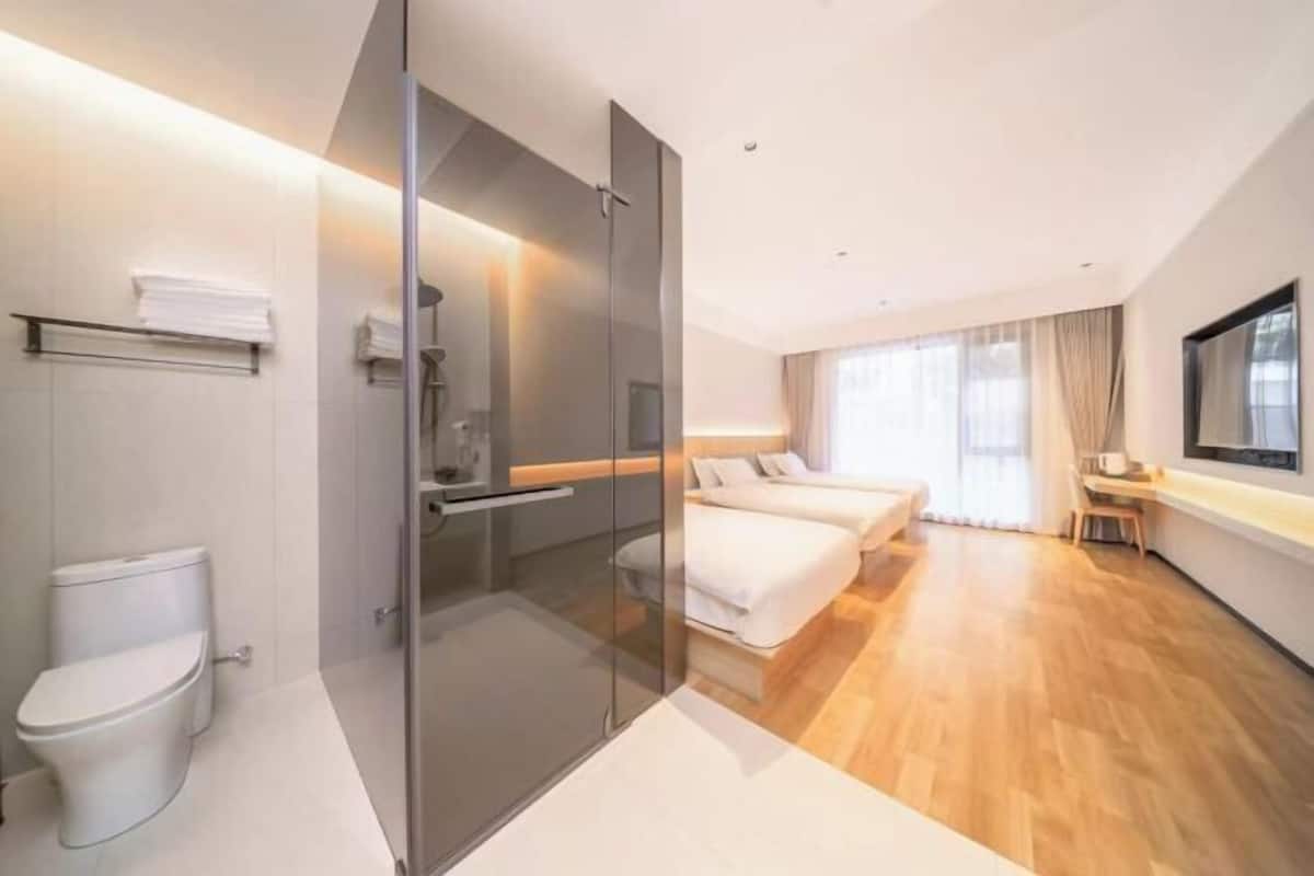 Una habitación de hotel moderna con cabina de ducha de vidrio, inodoro separado, cama, mesita de noche y un ventanal grande.