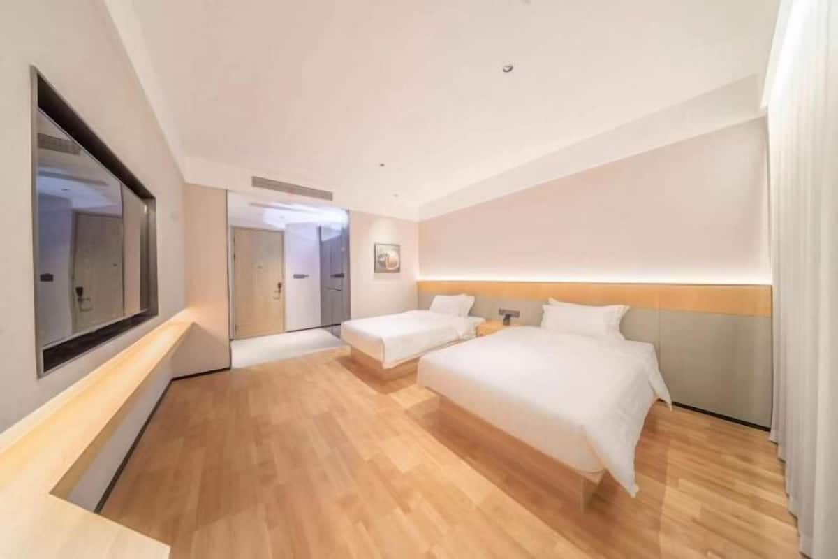 Una habitación de hotel moderna con una cama grande, una cama individual, una mesita de noche, un espejo y piso de madera.