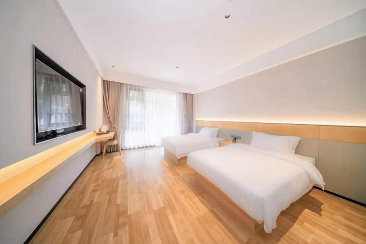 Habitación de hotel con dos camas, un ventanal con cortinas, un televisor de pantalla plana y suelo de madera.