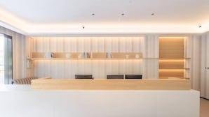 Una moderna reception con design bianco e in legno, una porta in vetro a sinistra e una mensola a parete con oggetti decorativi.