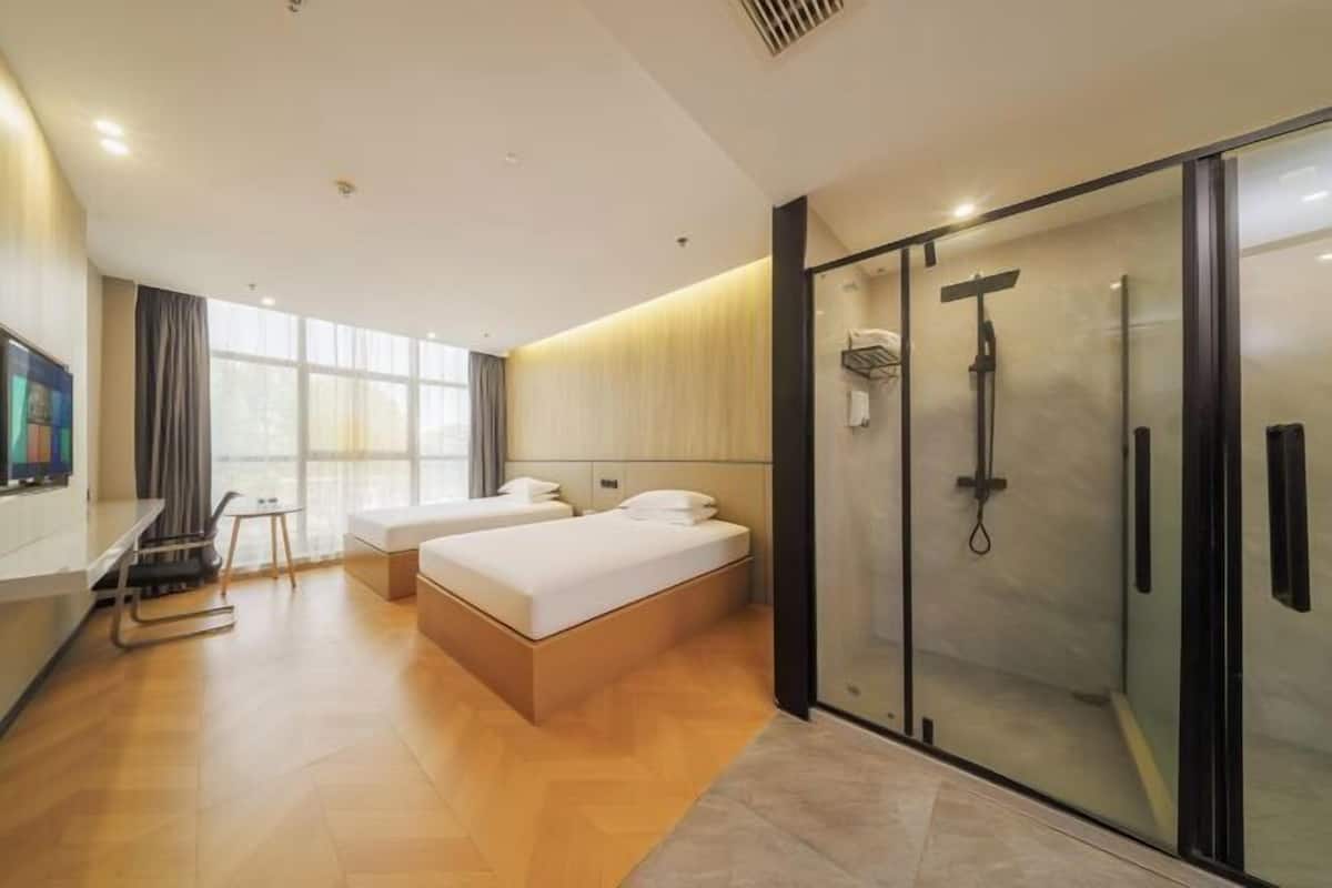 Una habitación de hotel moderna con una cama grande, zona de ducha y un área de descanso con televisión.