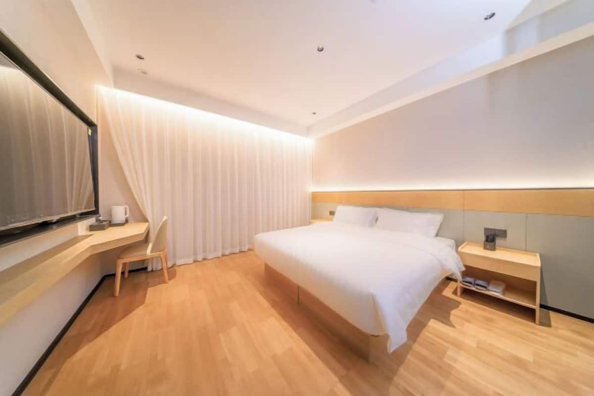 Una habitación de hotel moderna con una cama grande, una mesita de noche, una silla y un ventanal con cortinas.