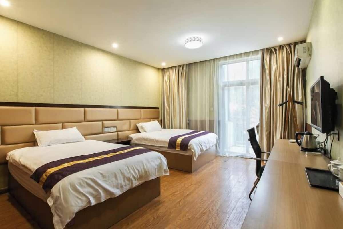 Habitación de hotel con dos camas, un escritorio de madera, un televisor y una ventana con cortinas.