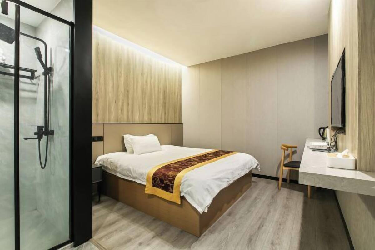 Una habitación de hotel moderna con cama, ducha, tocador con espejo y una mesita.