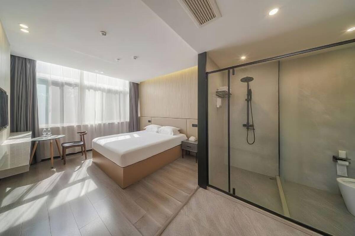 Habitación de hotel moderna con una cama grande, un escritorio con silla, cabina de ducha de vidrio y vistas al exterior.