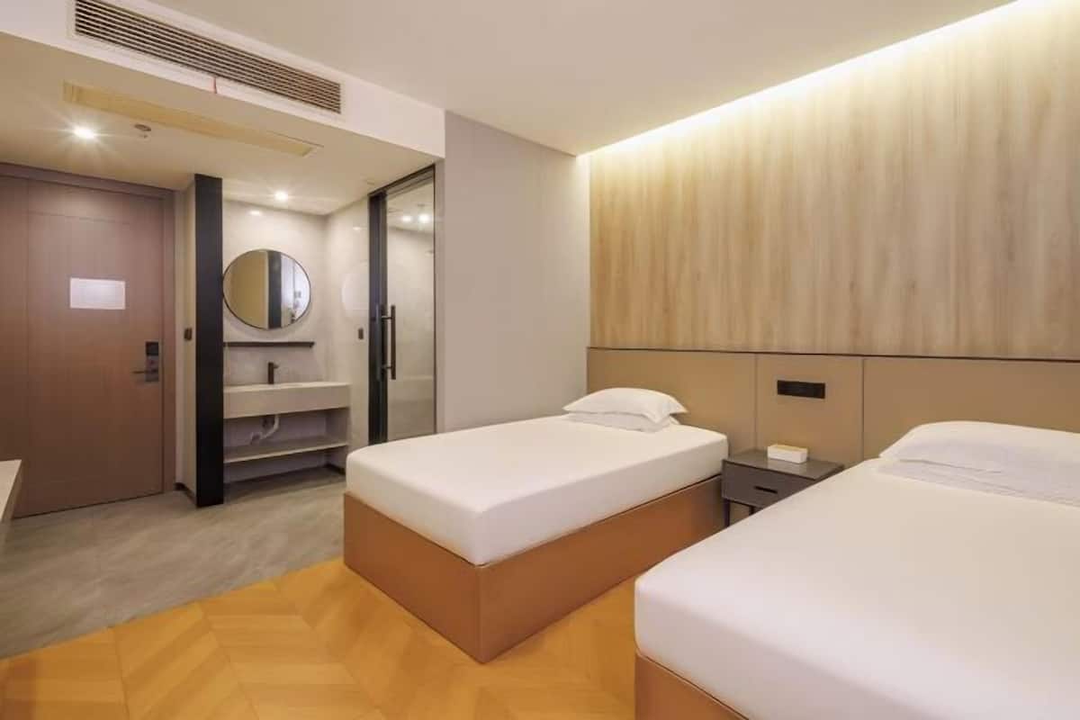 Habitación de hotel con dos camas, piso de madera, un espejo, un lavamanos y cabecera de madera.