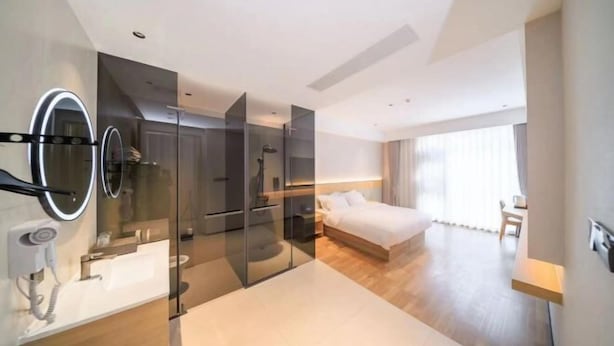 Una camera d'albergo moderna con cabina doccia in vetro, un letto grande, un comodino e una toeletta con specchio.