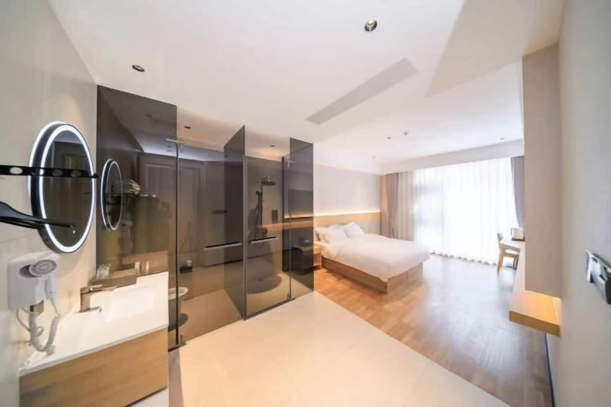 Una habitación de hotel moderna con ducha envuelta en vidrio, una cama grande, una mesita de noche y un tocador con espejo.