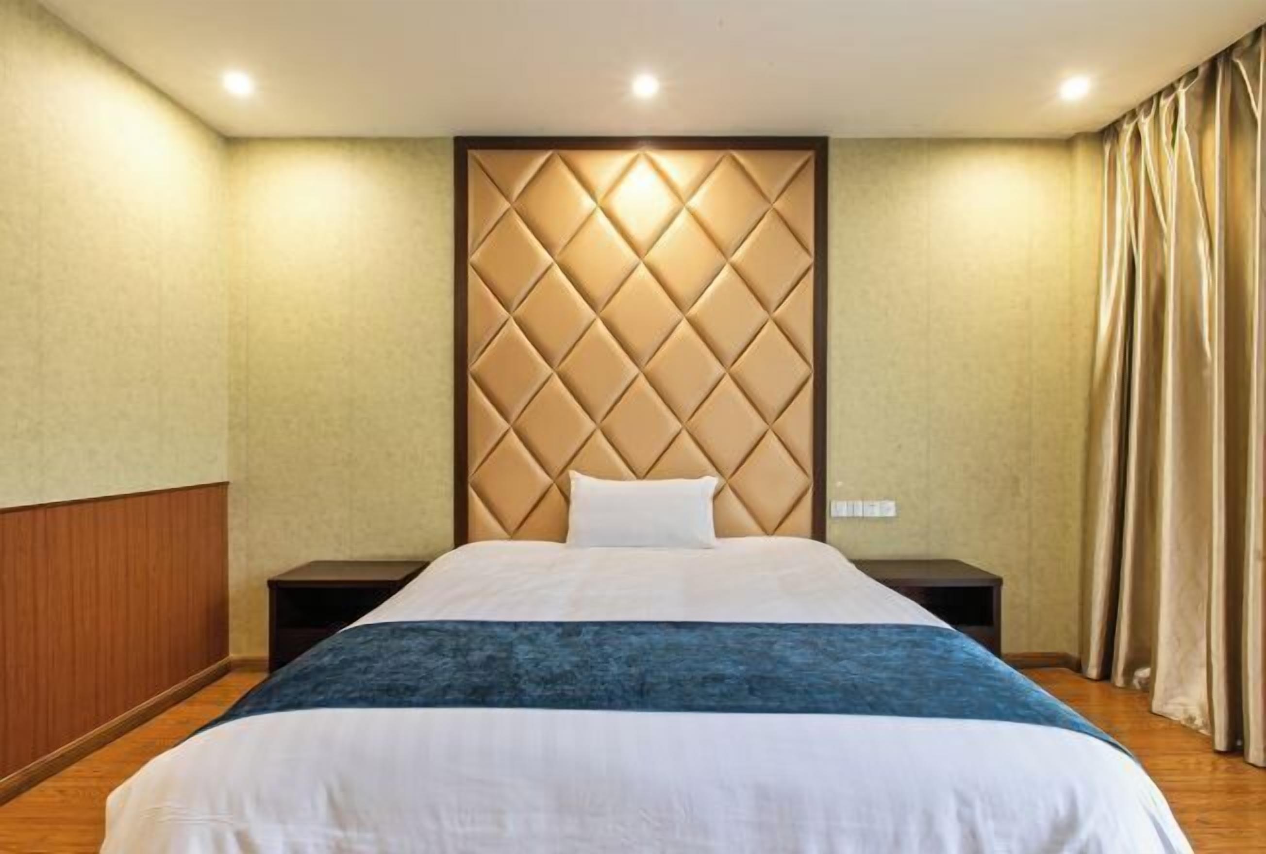 Una habitación de hotel con una cama grande, un cabecero acolchado, paneles de madera en las paredes y una mesita de noche.