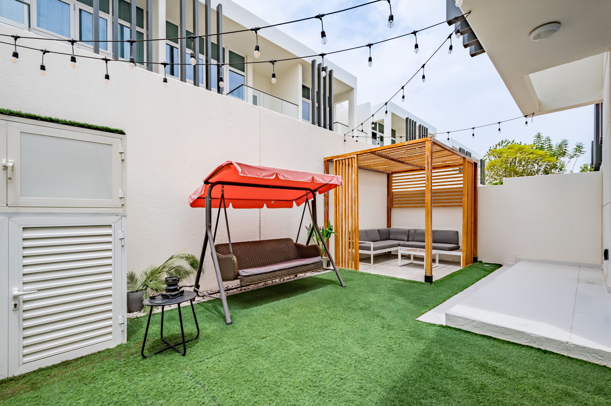 Een moderne buitenpatio met een schommel, een overdekte zithoek en een kleine tuin.