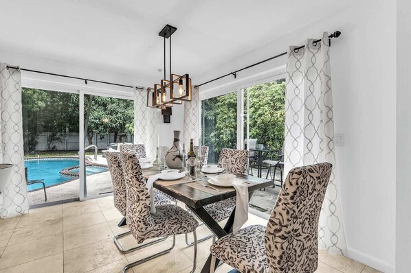 Uma área de refeições com vista para a piscina, cadeiras estampadas e um lustre moderno.