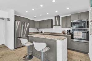 Uma cozinha moderna com eletrodomésticos de aço inoxidável, bancada de granito e dois bancos altos.