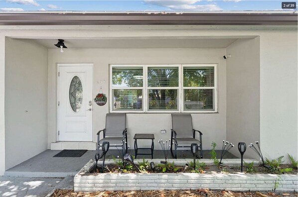 Welcome to this charming home with a cozy porch featuring a white door, a small table, and two chairs.