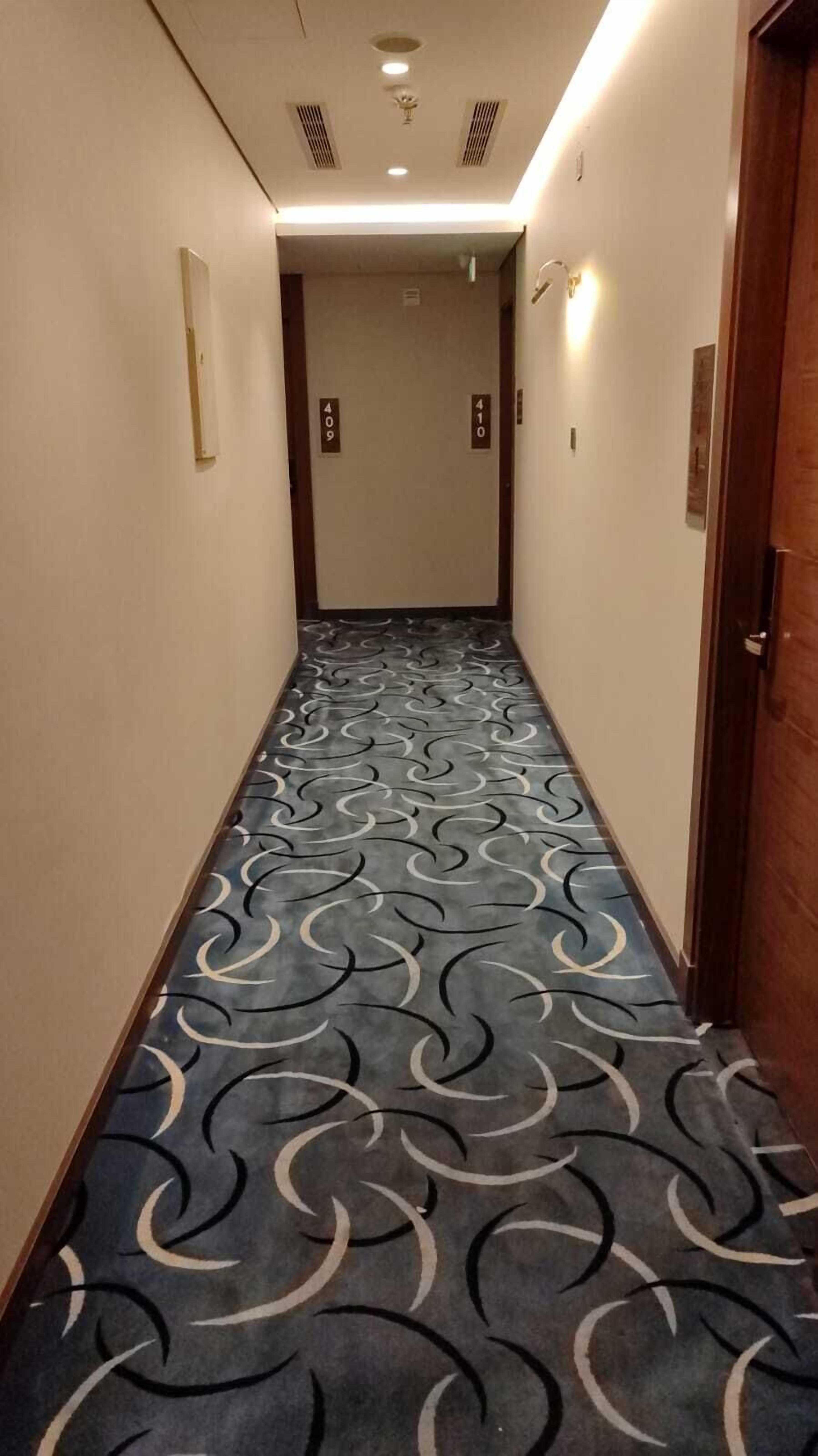 A hallway with a patterned carpet, numbered doors, and a wooden door on the right.