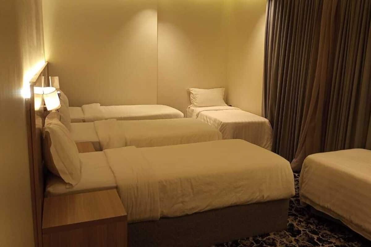 A hotel room with three single beds, a wooden nightstand, a lamp, and a curtain.
