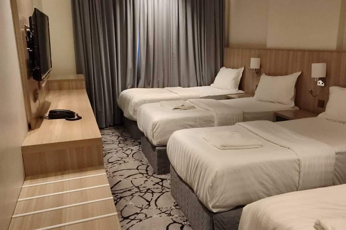 A hotel room with three beds, a TV, and a desk.
