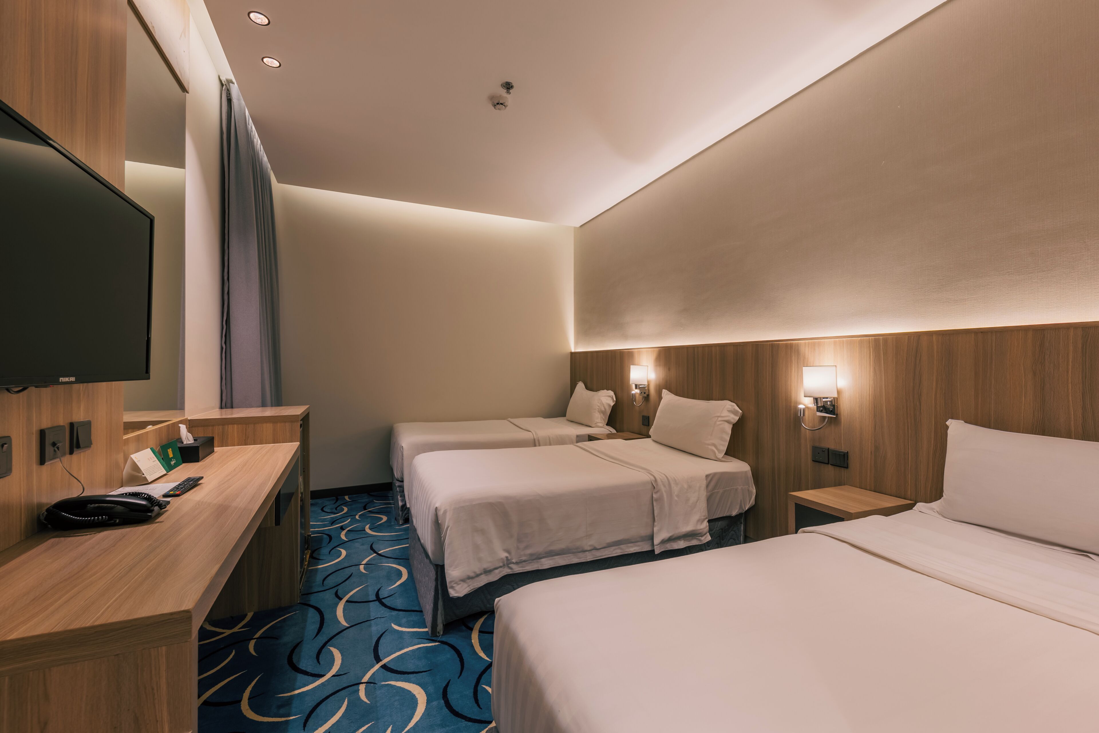 A hotel room with two beds, a desk, a flat-screen TV, and a bathroom.