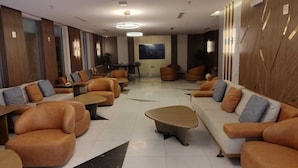 Un área de estar moderna con sofás y mesas dispuestas alrededor de una mesa de centro, un televisor de pantalla plana montado en la pared y un diseño de pared con motivos.