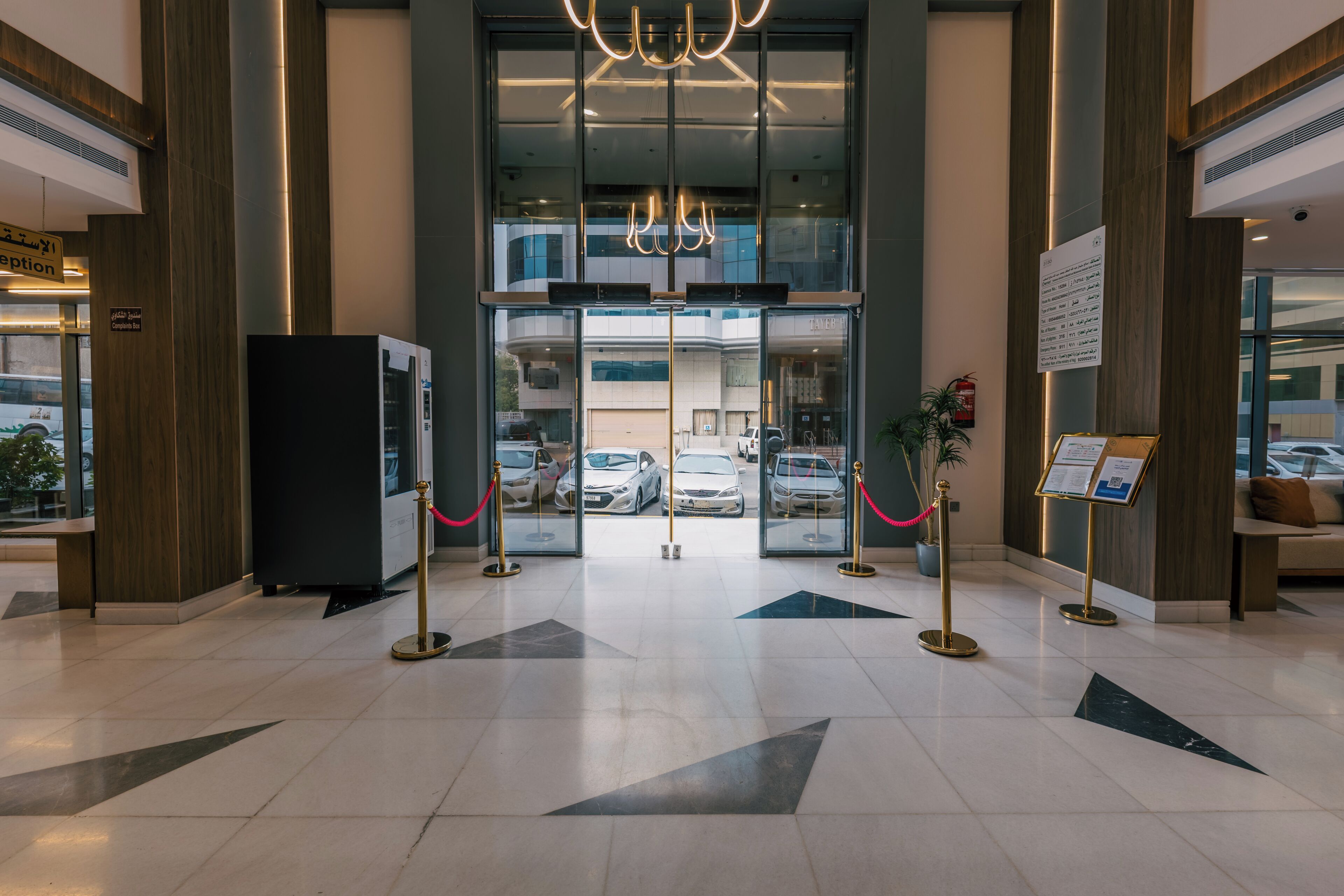 Un espace d’accueil d’hôtel doté d’une entrée avec une porte en verre, d’un comptoir de réception et d’une boîte à suggestions/réclamations.