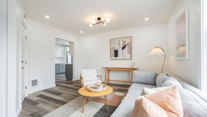 Ein modernes Wohnzimmer mit einer Couch, einem Couchtisch und einer Lampe. Im Hintergrund ist eine Küche zu sehen.