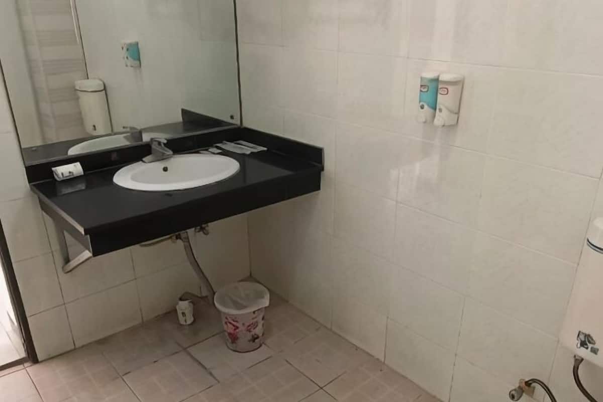 Une salle de bain avec un lavabo blanc, un plan de toilette noir, un miroir et une petite poubelle.