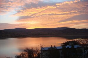 A lake with a sunset, hills in the background, and a building in the foreground.
