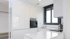 Una cocina moderna con armarios blancos, horno empotrado, hervidor de acero inoxidable y una ventana sobre el fregadero.