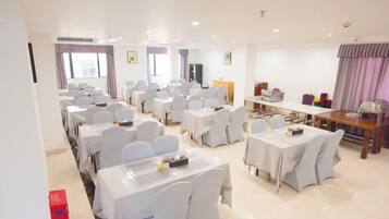 A conference room with multiple tables and chairs, a podium, and a large screen.