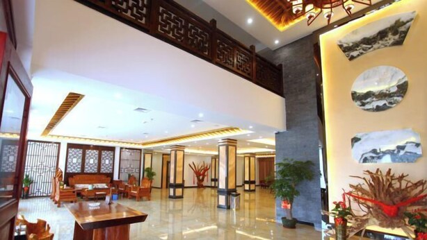A spacious lobby with a high ceiling, a central wooden table, and decorative plants. - Tongjing Hotel (Renhua)