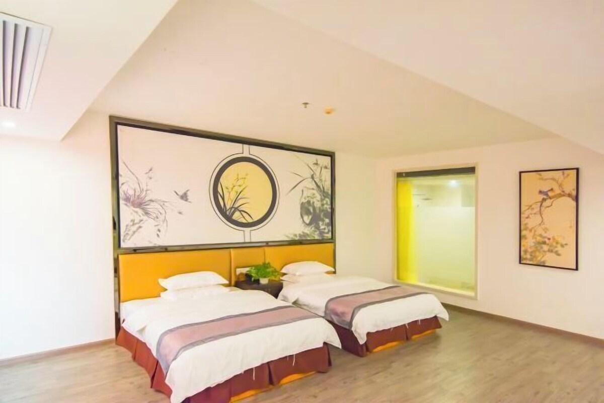 A room with two beds, a large window, and artwork on the walls.