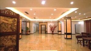 A spacious lobby with a polished marble floor, a large wooden-framed artwork on the left, and a modern reception desk with a potted plant. - Tongjing Hotel (Renhua)