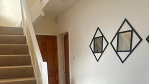 Una escalera que lleva a una puerta de madera, un pasillo con suelo de madera y dos adornos geométricos en la pared.