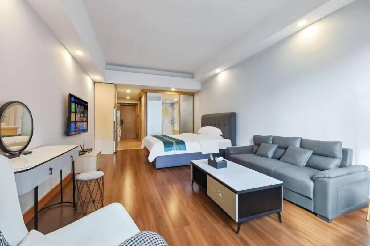 Et moderne hotelværelse med seng, grå sofa, hvid lænestol og et lille bord.