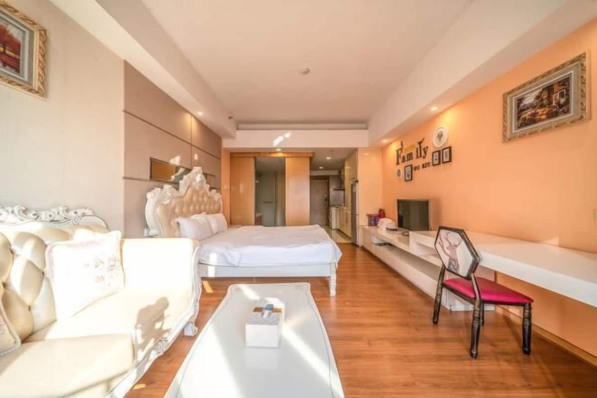 A modern hotel room with a bed, a sofa, a coffee table, and a TV.