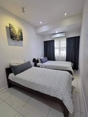 Een hotelkamer met twee bedden, een plafondlamp, een airconditioning en een schilderij aan de muur.