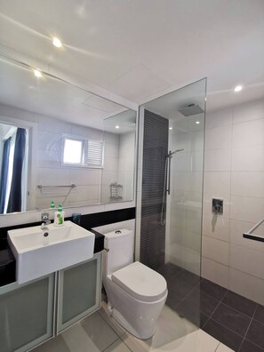 Een moderne badkamer met een douchecabine van glas, een wit wastafelmeubel en een toilet.